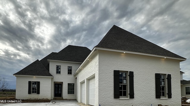 view of side of property featuring a garage, driveway, a shingled roof, and stucco siding