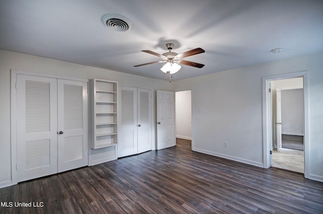 unfurnished bedroom with dark hardwood / wood-style floors, multiple closets, and ceiling fan