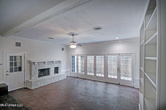 unfurnished living room with a stone fireplace, french doors, a textured ceiling, and ceiling fan