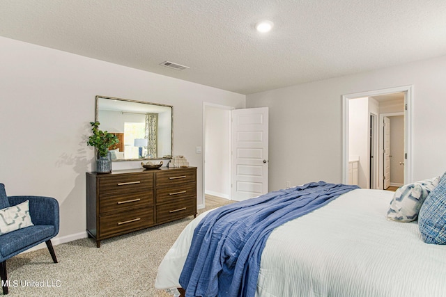 bedroom with light colored carpet, ensuite bath, and a textured ceiling