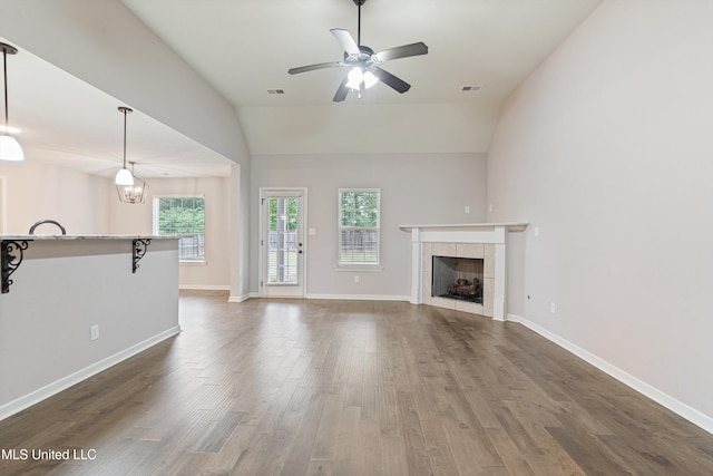 unfurnished living room with plenty of natural light, lofted ceiling, wood finished floors, a ceiling fan, and a fireplace