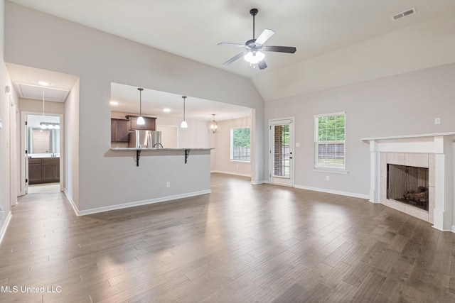 unfurnished living room featuring a ceiling fan, dark wood-type flooring, a tiled fireplace, baseboards, and lofted ceiling