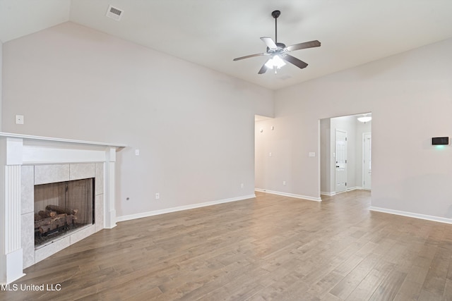 unfurnished living room featuring a ceiling fan, wood finished floors, high vaulted ceiling, a tiled fireplace, and baseboards