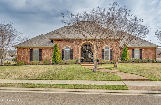 view of front of home with brick siding, roof with shingles, and a front yard