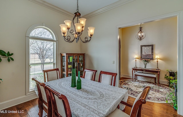 dining space featuring dark wood-type flooring, a notable chandelier, ornamental molding, and baseboards