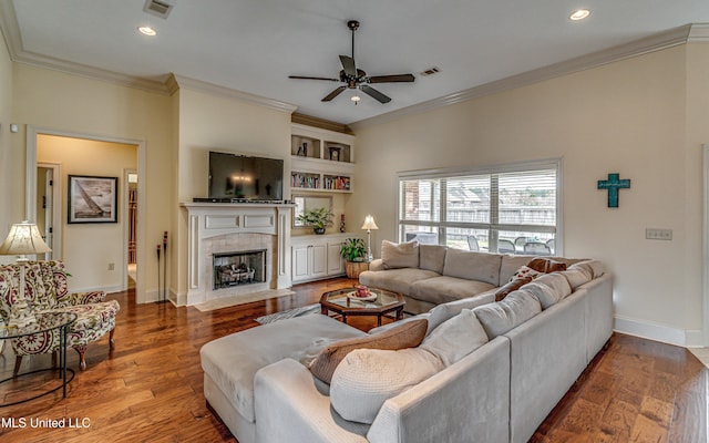 living area with crown molding, visible vents, a tiled fireplace, wood finished floors, and baseboards