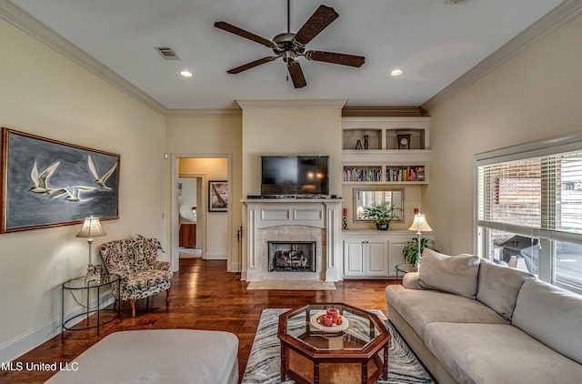 living area with visible vents, baseboards, a tiled fireplace, ornamental molding, and wood finished floors