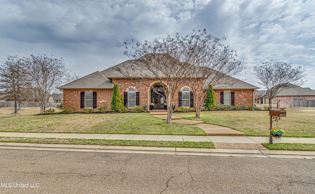 view of front facade featuring a shingled roof, a front yard, and brick siding