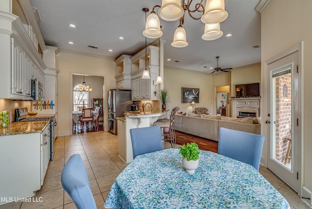 dining space with light tile patterned floors, ceiling fan with notable chandelier, a fireplace, visible vents, and crown molding