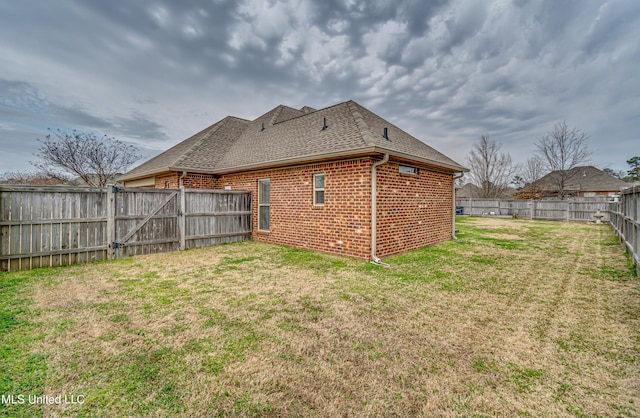 back of property with a shingled roof, brick siding, a lawn, and a fenced backyard