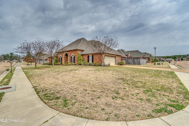 french country inspired facade featuring a garage, a front yard, brick siding, and driveway