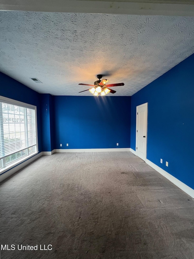 carpeted spare room featuring ceiling fan, a textured ceiling, visible vents, and baseboards