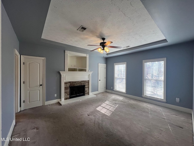 unfurnished living room with a tray ceiling, visible vents, a fireplace, and baseboards