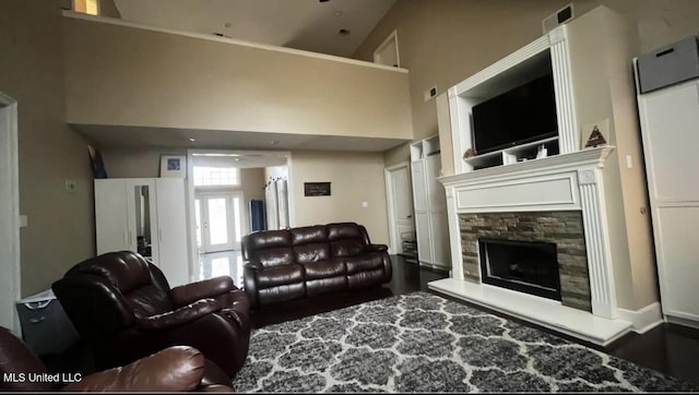 living area featuring visible vents, a stone fireplace, a high ceiling, and wood finished floors