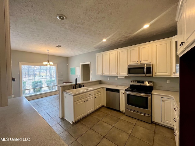 kitchen with light countertops, appliances with stainless steel finishes, white cabinets, a sink, and a peninsula