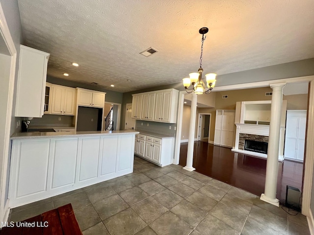 kitchen with a notable chandelier, a peninsula, a fireplace, visible vents, and decorative columns