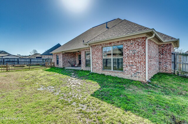 rear view of house featuring a lawn, a fenced backyard, brick siding, and a shingled roof