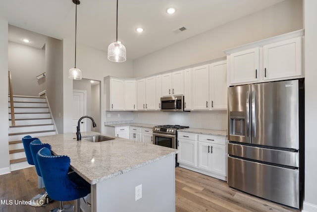 kitchen with sink, an island with sink, white cabinetry, light hardwood / wood-style floors, and stainless steel appliances