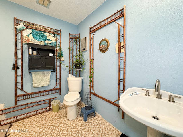 bathroom with toilet, a textured ceiling, and sink