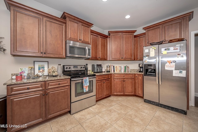 kitchen with brown cabinets, light tile patterned floors, appliances with stainless steel finishes, light stone countertops, and recessed lighting