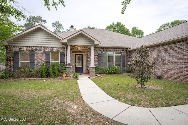 view of front of house featuring a shingled roof, a chimney, brick siding, and a front yard