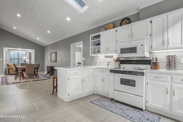 kitchen with white appliances, white cabinetry, lofted ceiling with skylight, tasteful backsplash, and kitchen peninsula