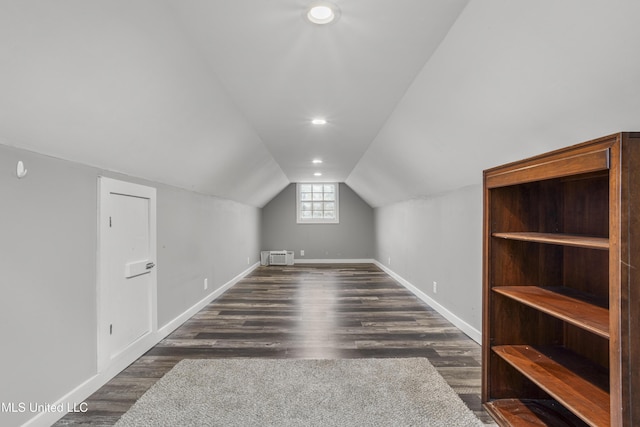 additional living space with lofted ceiling, a wall unit AC, and dark hardwood / wood-style flooring