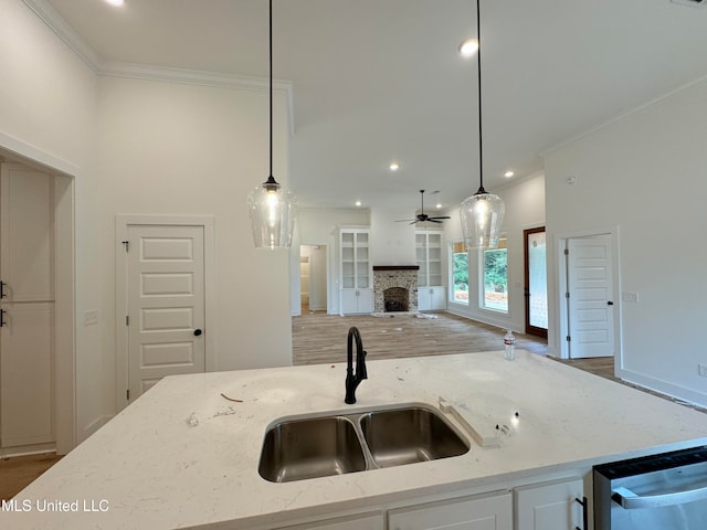 kitchen with a fireplace, decorative light fixtures, sink, light stone countertops, and a center island with sink