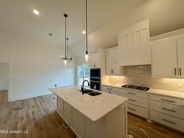 kitchen with black oven, decorative light fixtures, white cabinetry, sink, and a kitchen island with sink