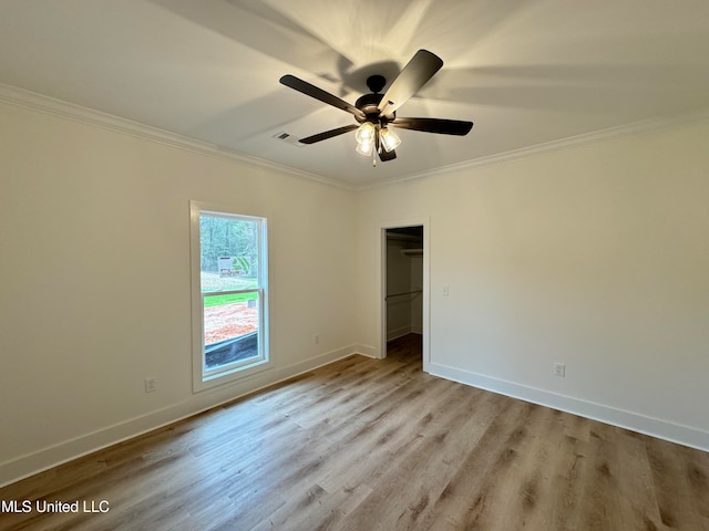 unfurnished bedroom featuring crown molding, a walk in closet, a closet, and ceiling fan