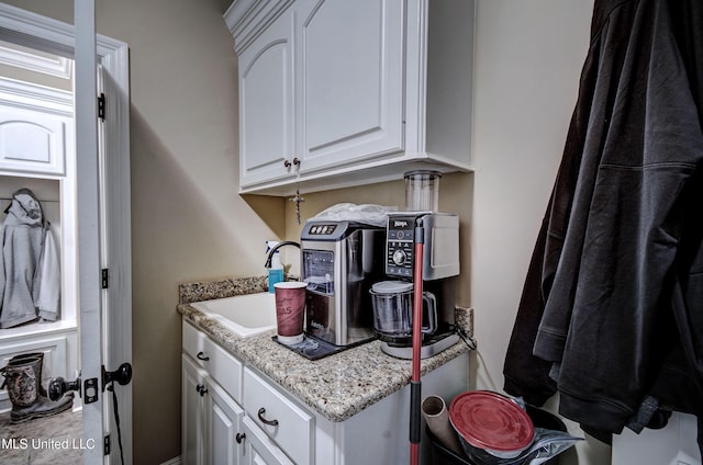 kitchen featuring light stone counters, white cabinetry, and a sink