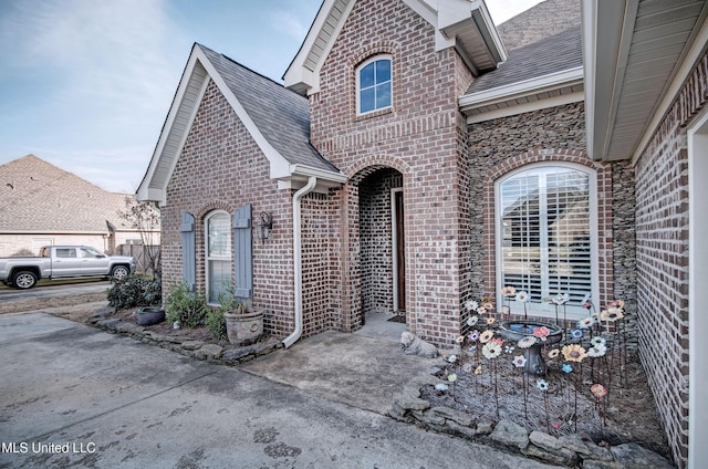 exterior space featuring brick siding and roof with shingles