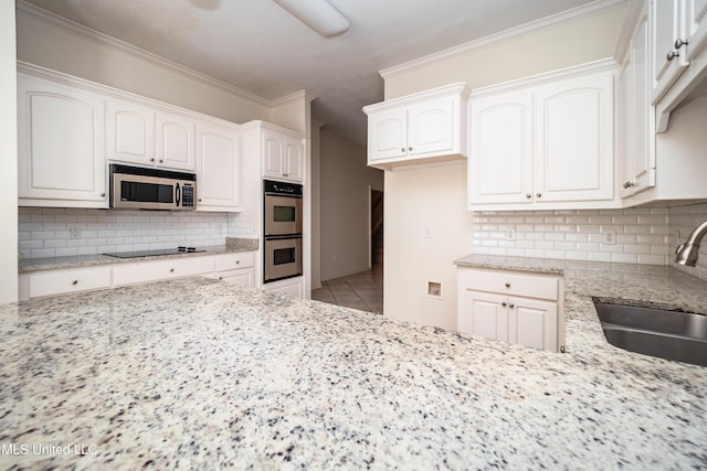 kitchen featuring backsplash, crown molding, light stone countertops, stainless steel appliances, and a sink