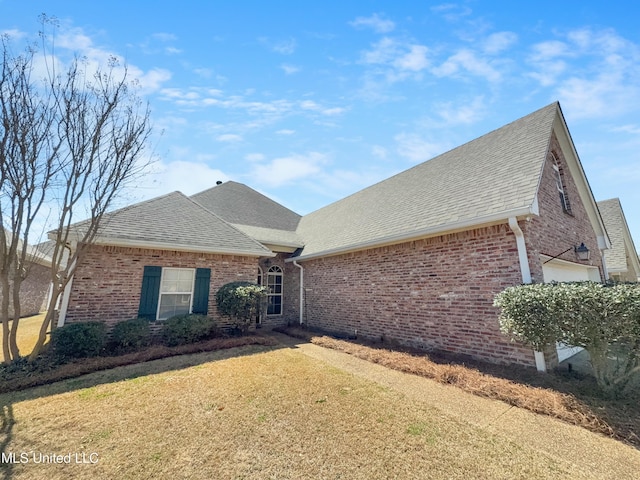 view of front of property featuring brick siding, a front yard, and roof with shingles