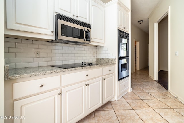 kitchen featuring tasteful backsplash, stainless steel microwave, black electric stovetop, double oven, and light tile patterned floors