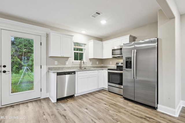 kitchen featuring appliances with stainless steel finishes, sink, light hardwood / wood-style floors, white cabinets, and light stone counters