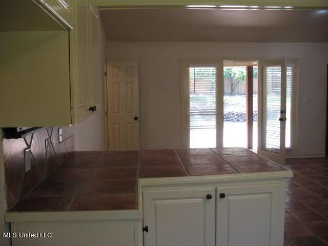 kitchen featuring a peninsula, tile countertops, dark tile patterned floors, and white cabinetry