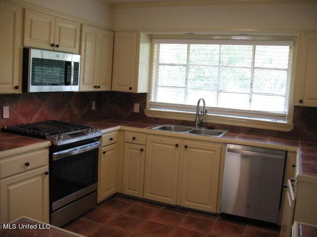 kitchen with stainless steel appliances, tasteful backsplash, a sink, and tile countertops