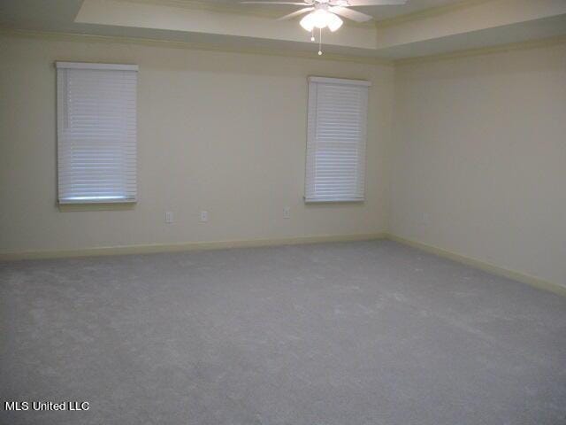 empty room featuring a ceiling fan, baseboards, a tray ceiling, and carpet floors