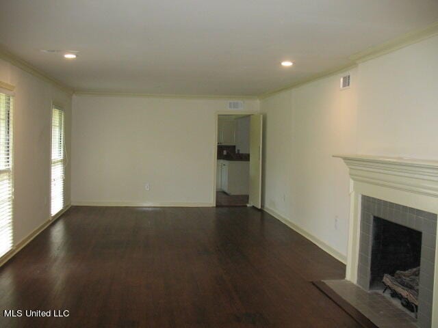 unfurnished living room with ornamental molding, a tiled fireplace, and dark wood-type flooring