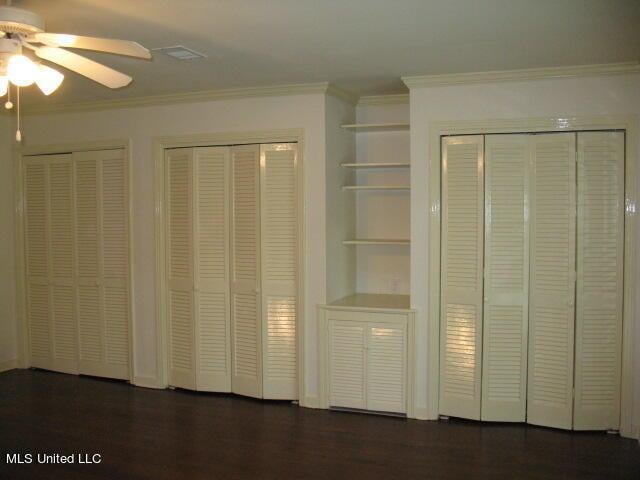 unfurnished bedroom featuring two closets, ornamental molding, dark wood-style floors, and a ceiling fan