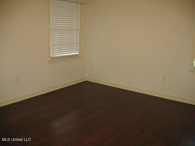 spare room featuring dark wood-style flooring and baseboards