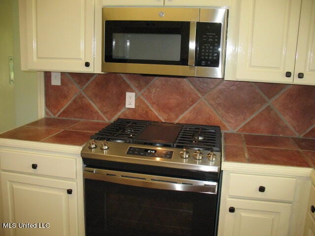 kitchen with appliances with stainless steel finishes, white cabinetry, and backsplash