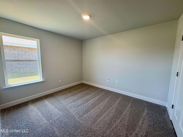 empty room featuring dark colored carpet and baseboards