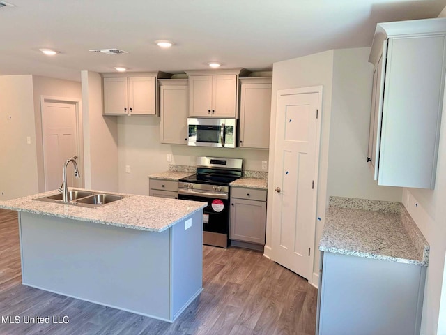 kitchen featuring an island with sink, light wood-style flooring, visible vents, stainless steel appliances, and a sink