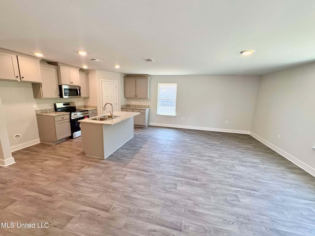 kitchen with an island with sink, appliances with stainless steel finishes, wood finished floors, a sink, and baseboards