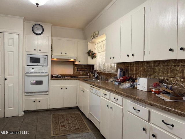 kitchen featuring under cabinet range hood, white appliances, a sink, white cabinets, and tasteful backsplash