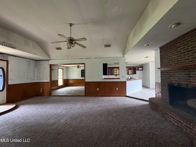 unfurnished living room with lofted ceiling, wooden walls, light carpet, a fireplace, and ceiling fan