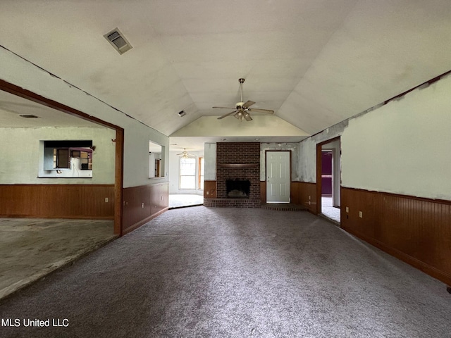 unfurnished living room featuring wood walls, carpet flooring, vaulted ceiling, and ceiling fan