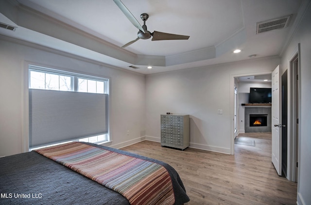 bedroom featuring a tray ceiling, ceiling fan, crown molding, and light hardwood / wood-style floors